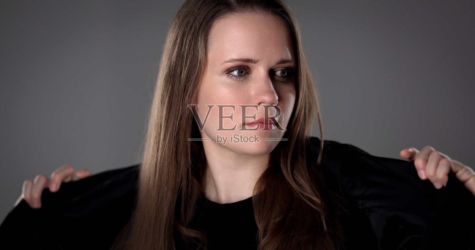 年轻女子在灰色背景前调整黑色夹克，看向别处照片摄影图片