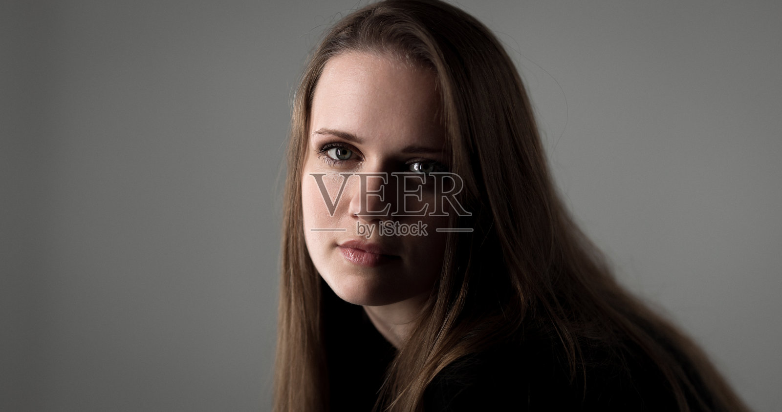 一位长棕色头发的年轻女子在影棚的灰色背景前摆姿势照片摄影图片