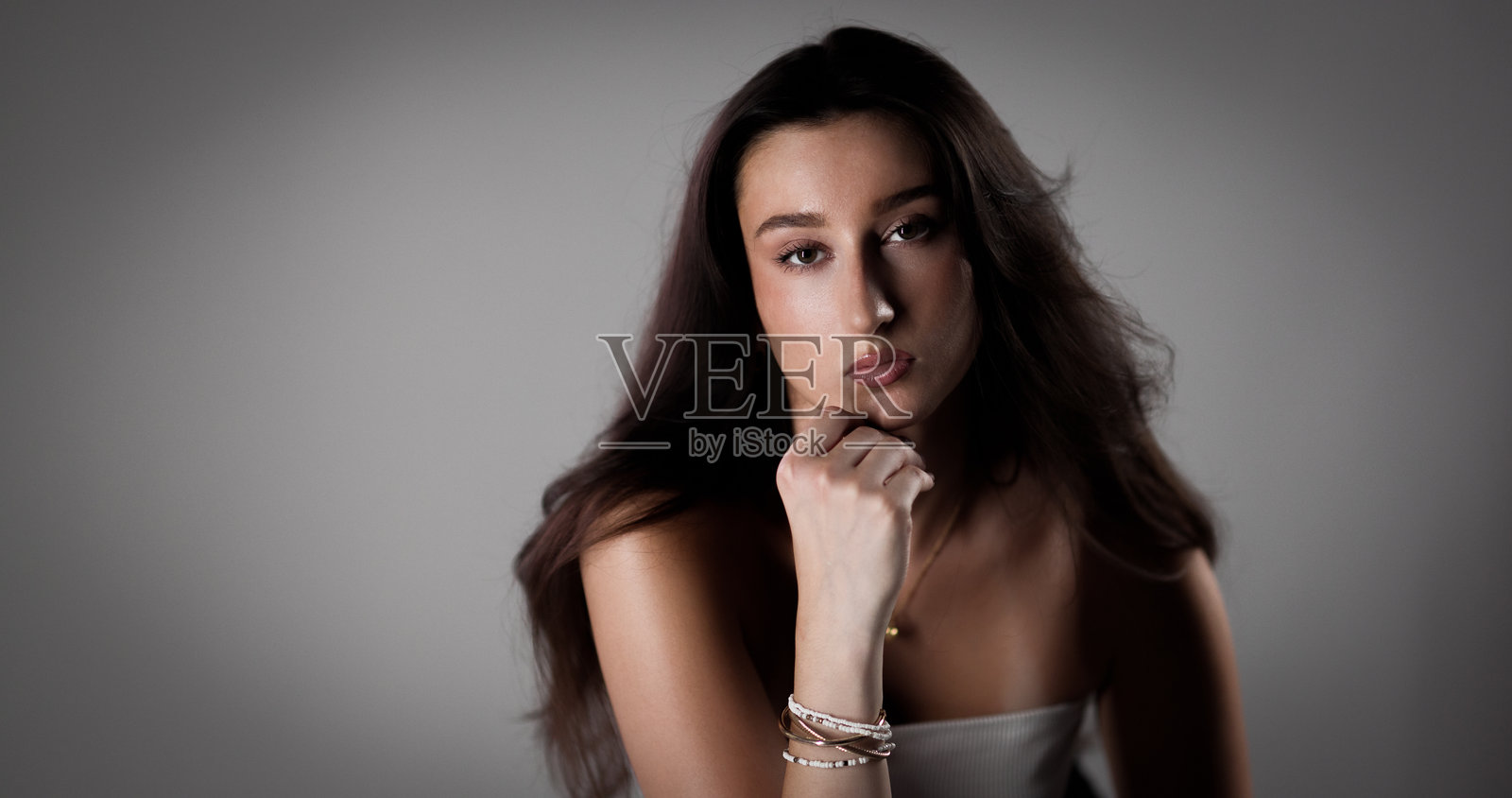 一位年轻女子手托着下巴，在灰色背景的影棚里摆姿势照片摄影图片
