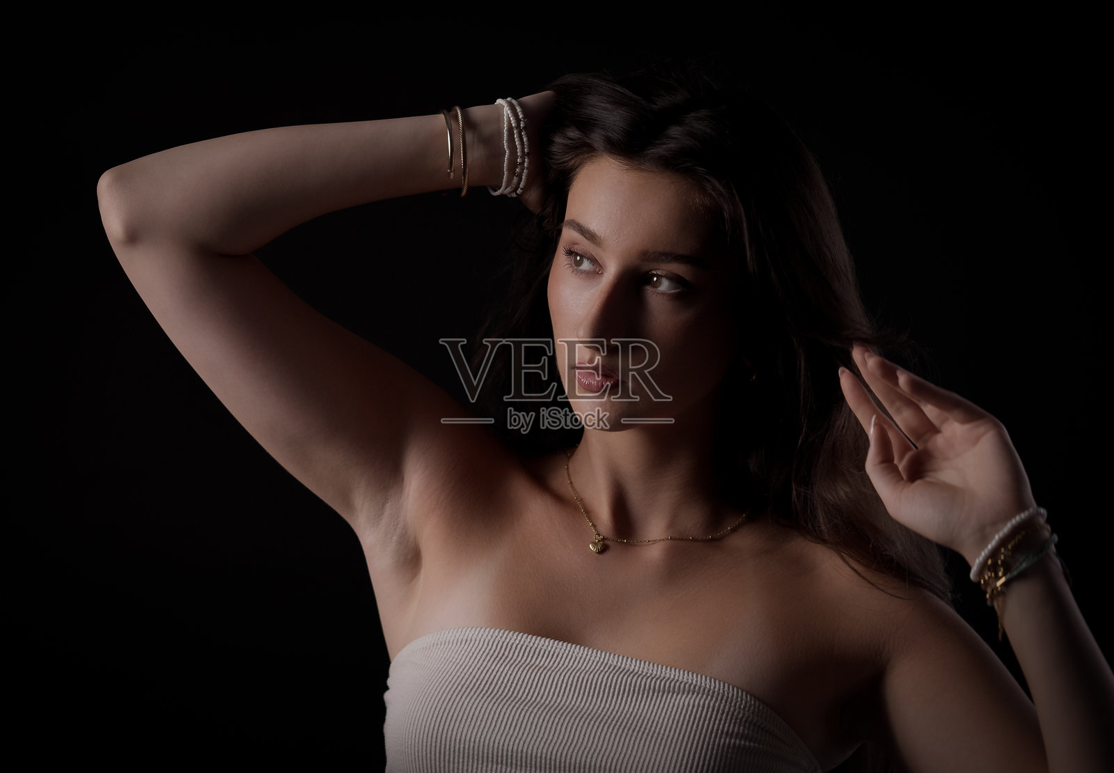 年轻女子在黑色背景前摆姿势，手撩头发，手臂高举照片摄影图片