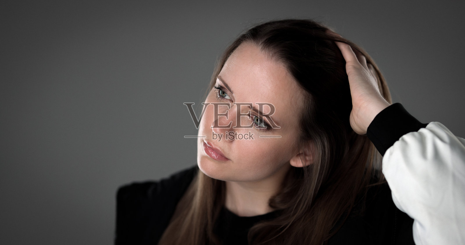 年轻女子在灰色背景下思考并整理头发照片摄影图片