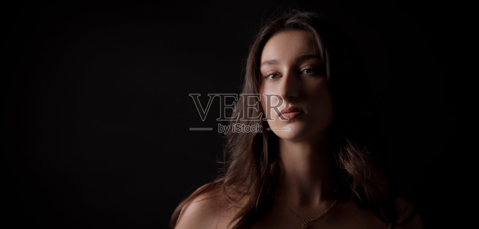 年轻女子在黑色背景前摆姿势，表情严肃，露出肩膀照片摄影图片