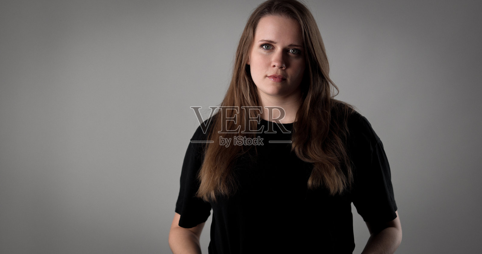 留着长棕发的严肃年轻女子在灰色背景的影棚中摆姿势照片摄影图片