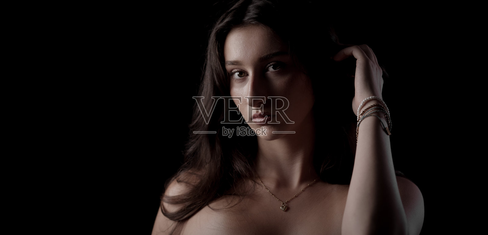 长发女子戴着手镯和项链，在黑色背景前触碰头部摆拍照片摄影图片