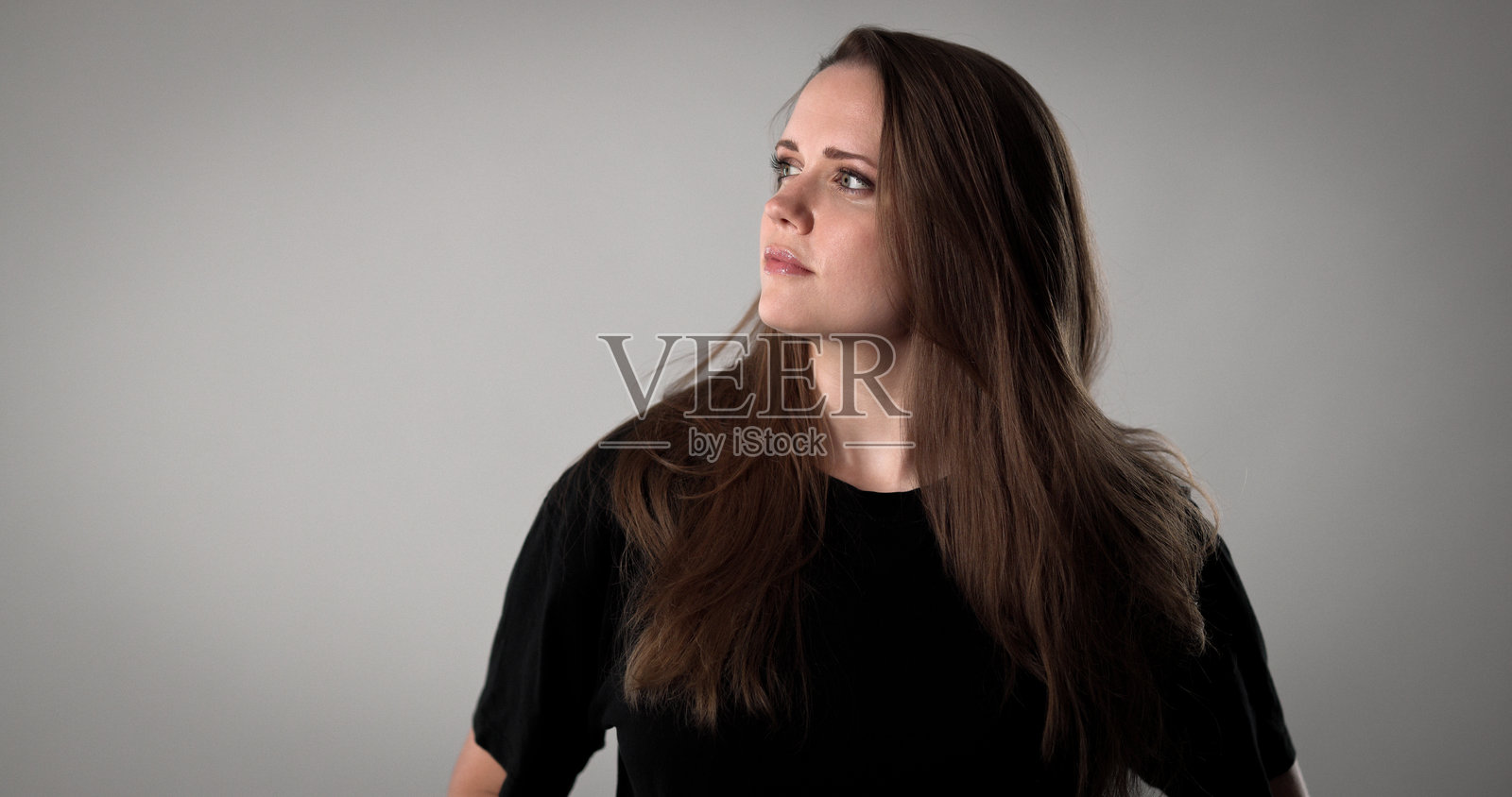 年轻女子在灰色背景下抬头沉思，表情若有所思照片摄影图片