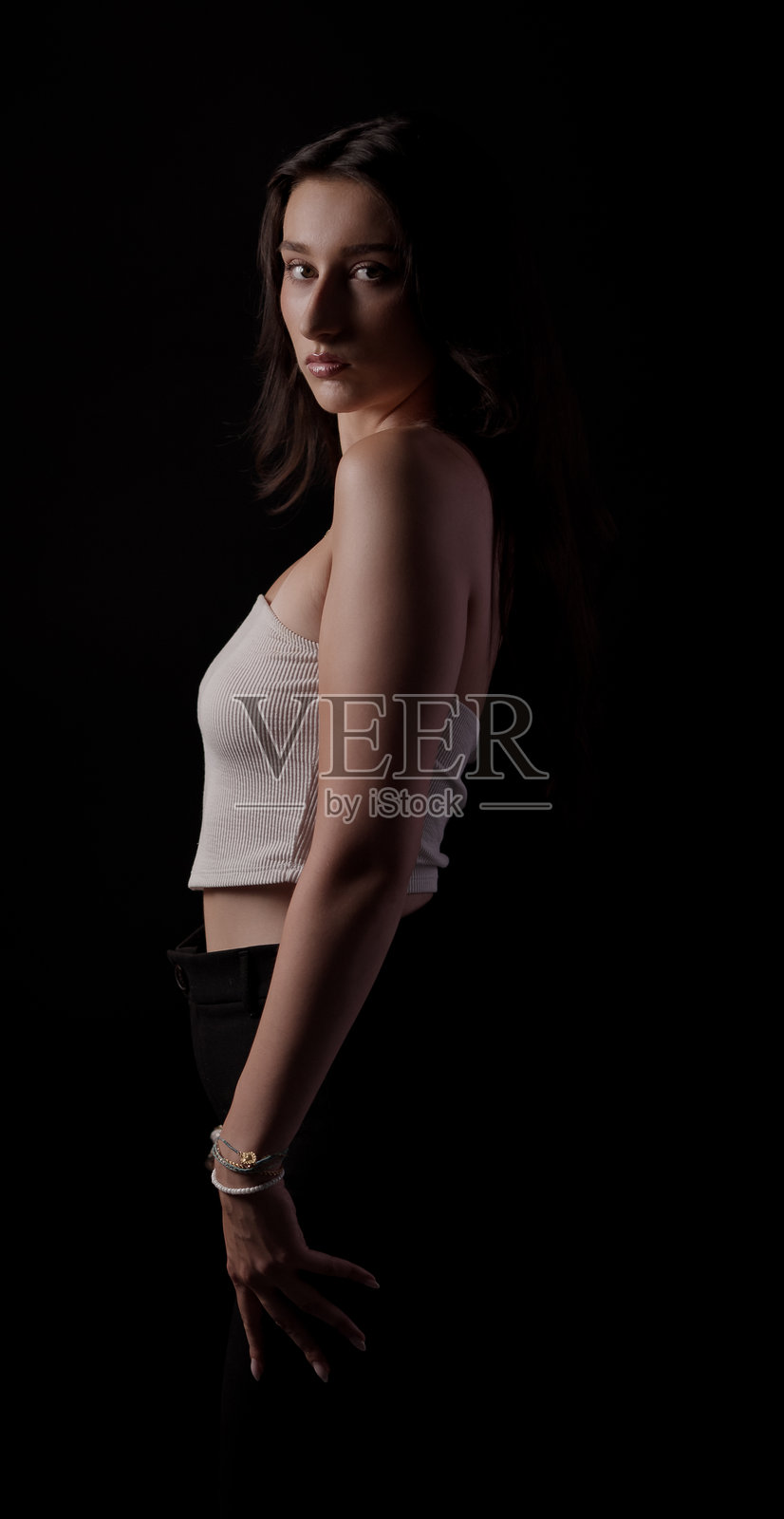 年轻女子在黑色背景的影棚内摆姿势，身穿白色上衣和黑色裤子照片摄影图片