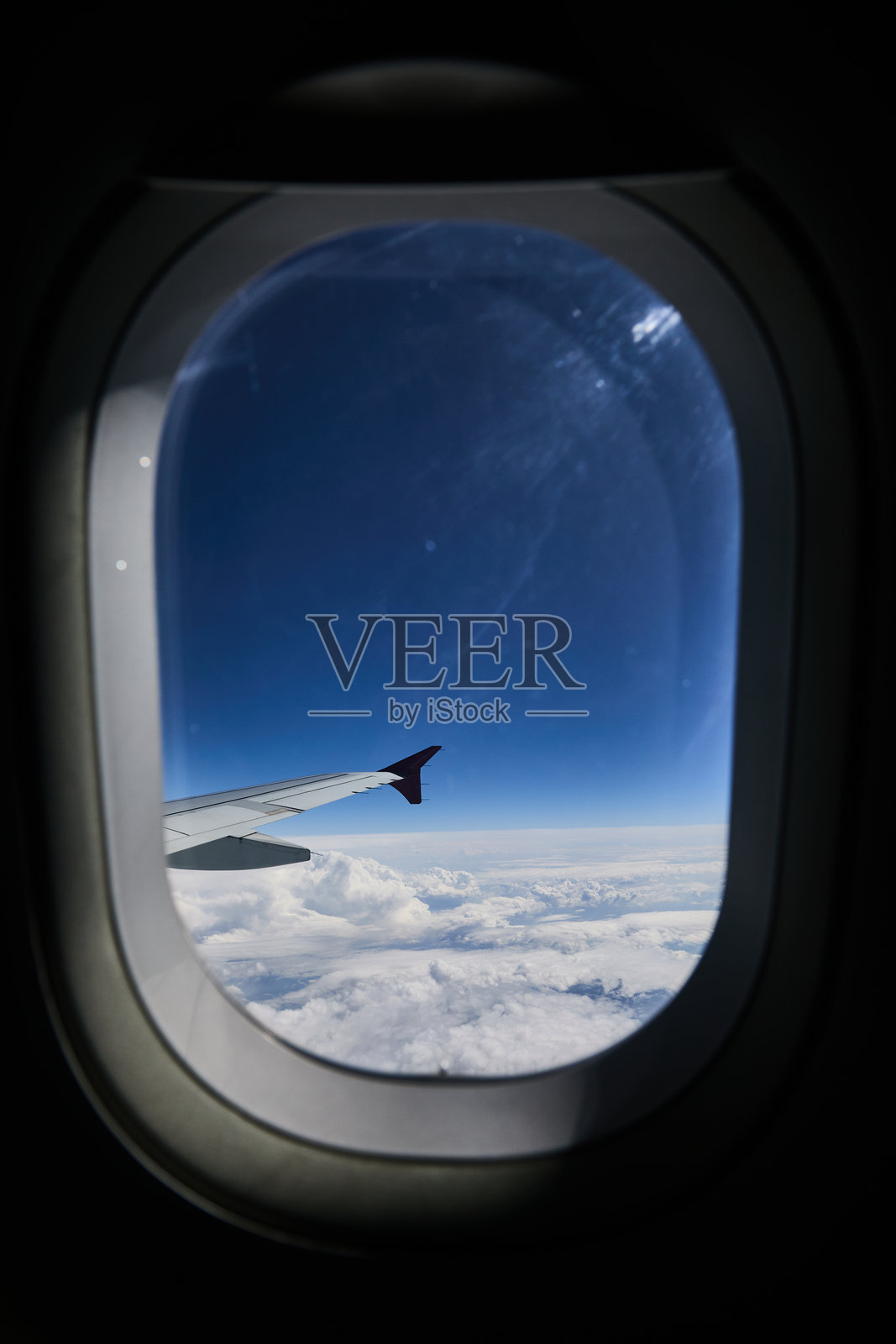 从飞机舷窗望出去，云层之上，机翼尖端在画面中，蓝天与地平线照片摄影图片