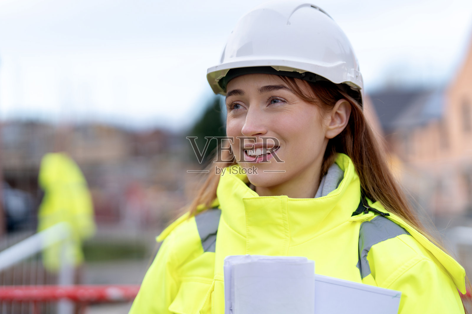 一位留着长发、戴着安全帽、手持建筑图纸的美丽女建筑师在项目规划中微笑的肖像照片摄影图片