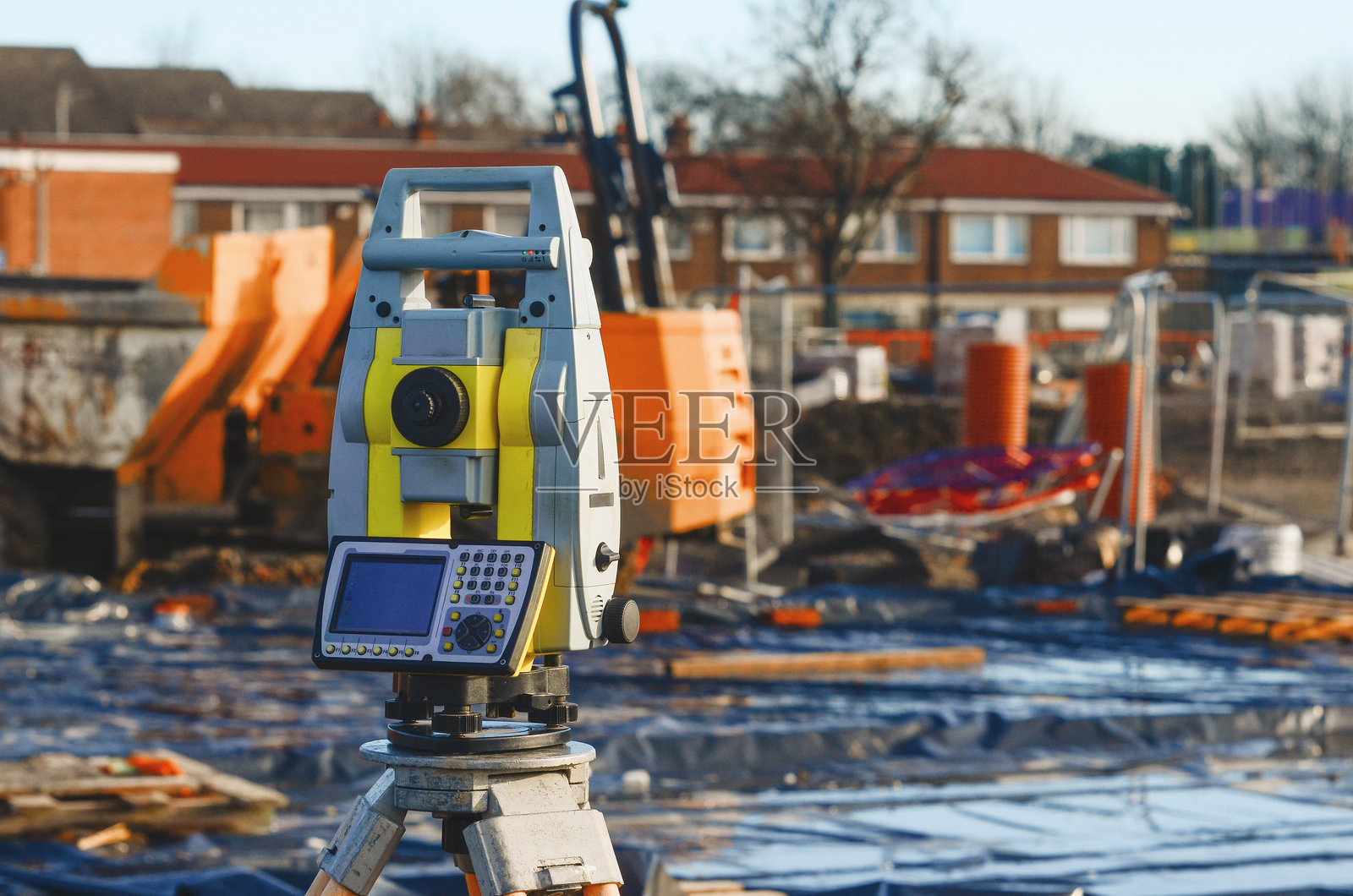 土地测量设备，如经纬仪或全站仪，安装在三脚架上，位于建筑工地上，由土地测量员进行测量，背景为建筑活动。照片摄影图片