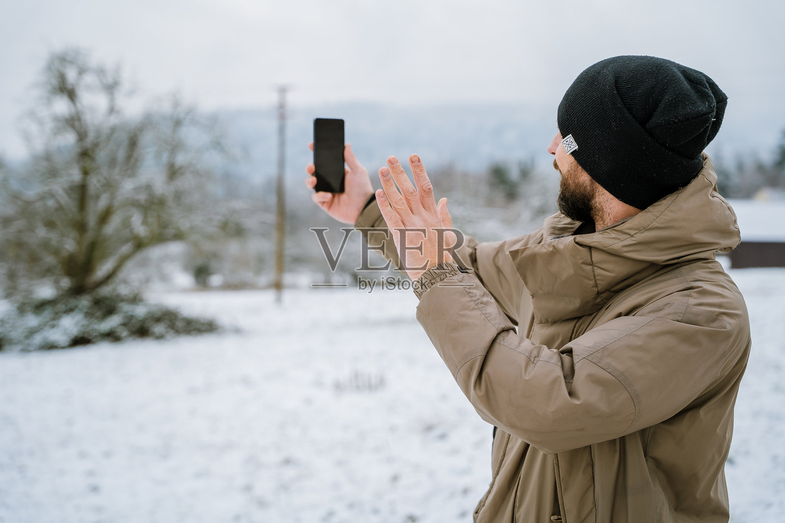 雪地公园里年轻男子肖像，他正在使用智能手机，冬季概念。照片摄影图片