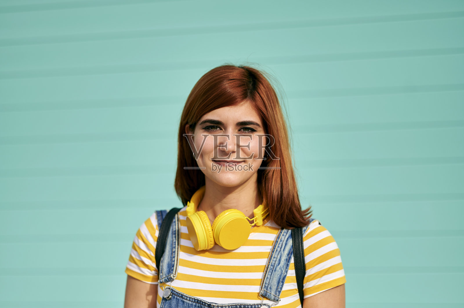 年轻女子戴着耳机，在绿松石色的墙壁前摆姿势照片摄影图片