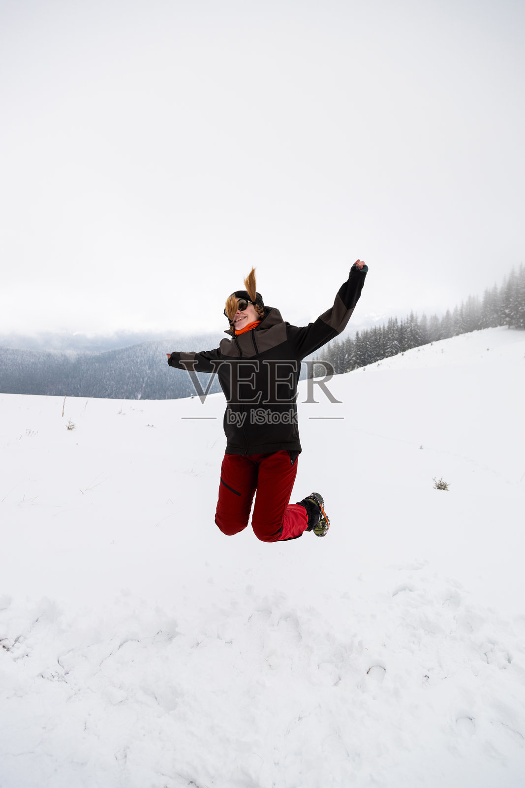 在多云的天空下，于宁静的山脉环绕的雪景中，快乐地跳跃照片摄影图片