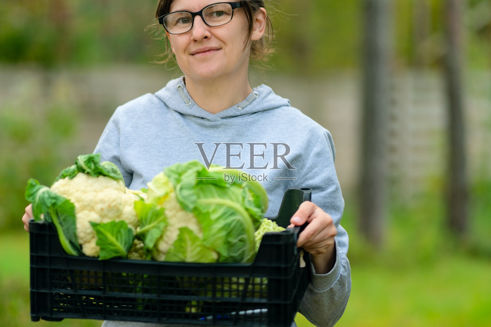 一位微笑着的女性农夫，手中拿着一盒新鲜的菜花收成。照片摄影图片