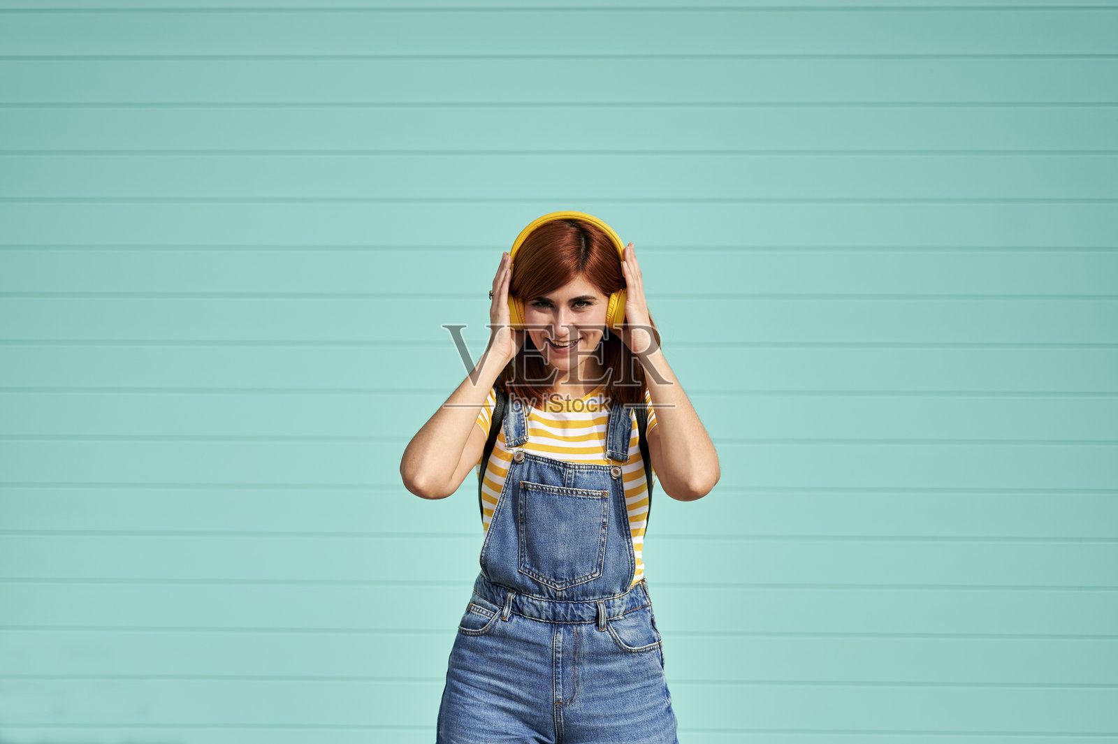 一位快乐的女士戴着耳机，在浅蓝色背景下听音乐照片摄影图片