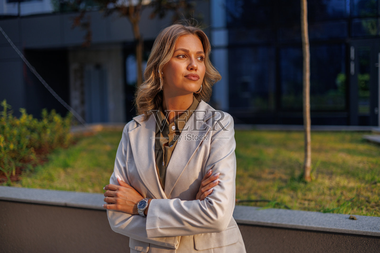 一位自信的女商人，身处城市背景中，双臂交叉，面向夕阳，眺望远方，专注于未来照片摄影图片