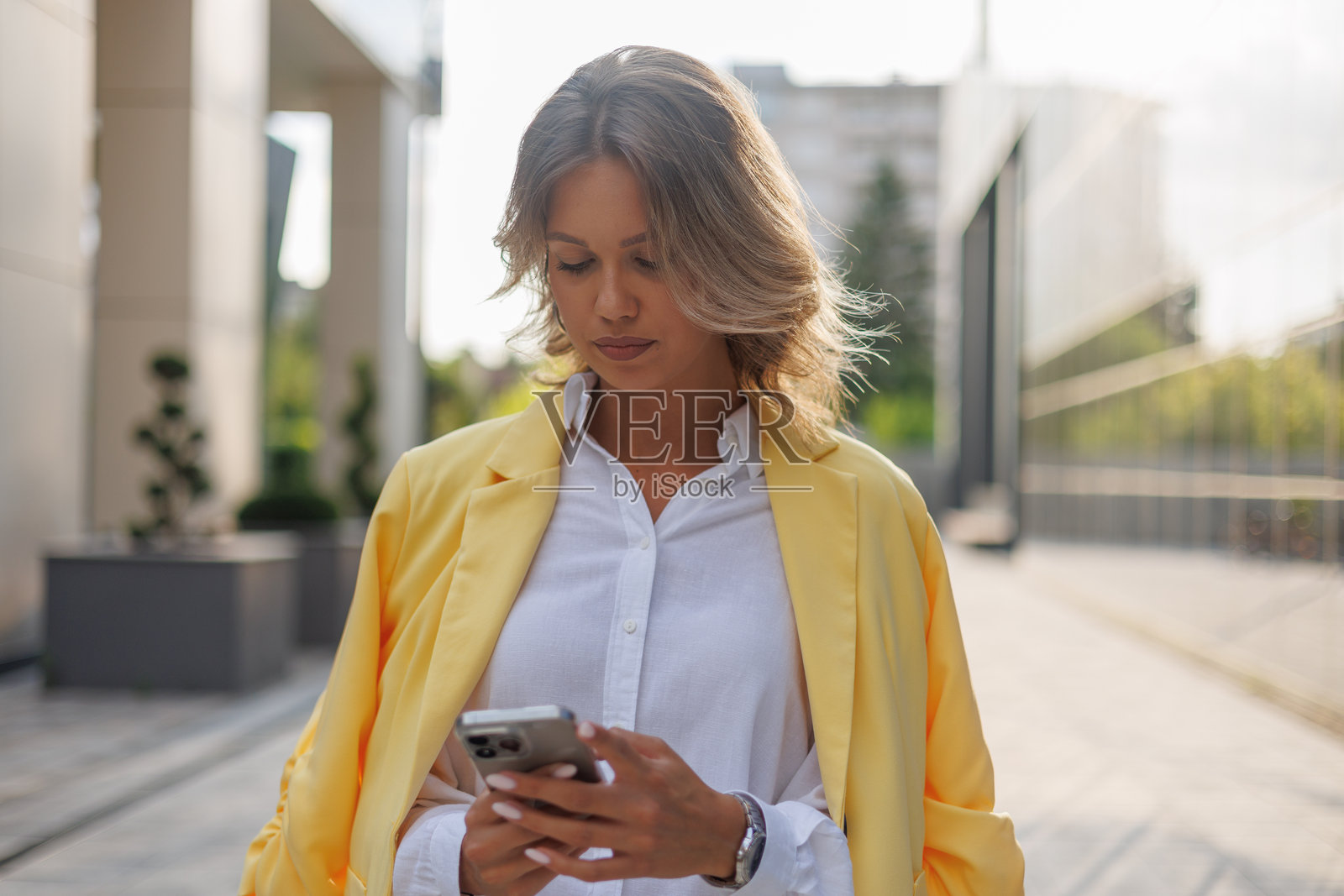 一位身穿黄色西装外套的职业女性在户外使用智能手机，在城市环境中与科技互动照片摄影图片