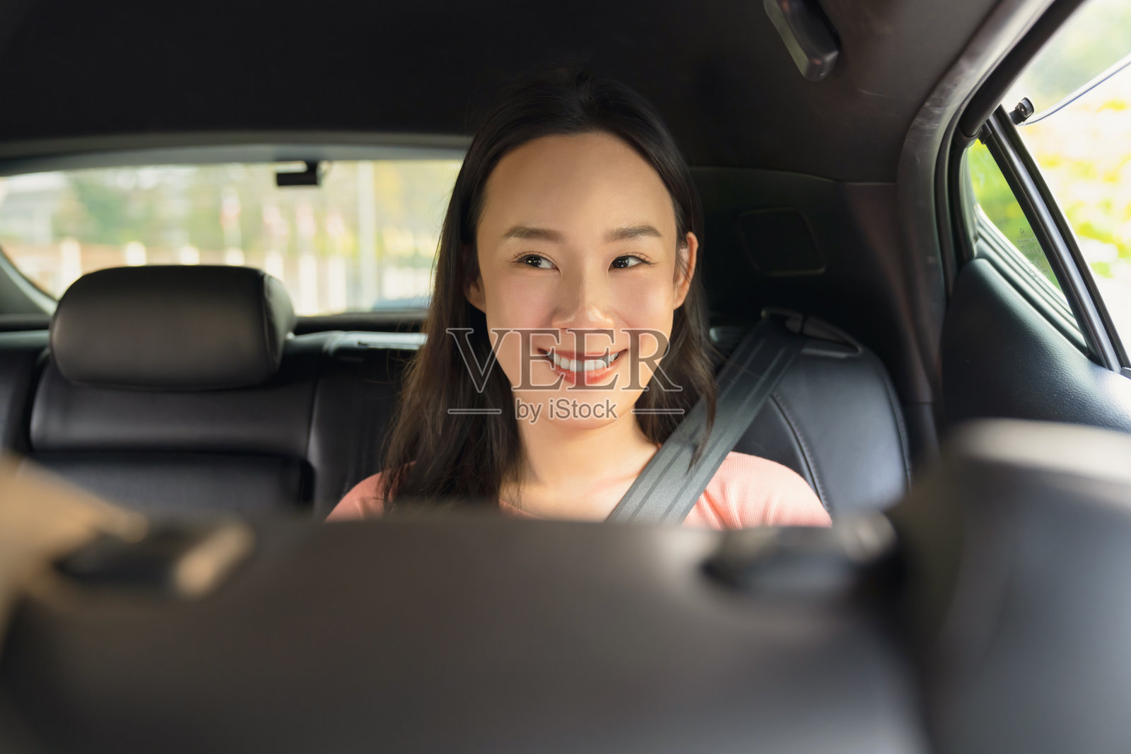 一位微笑的亚洲女商人正坐在私家车里使用智能手机。照片摄影图片