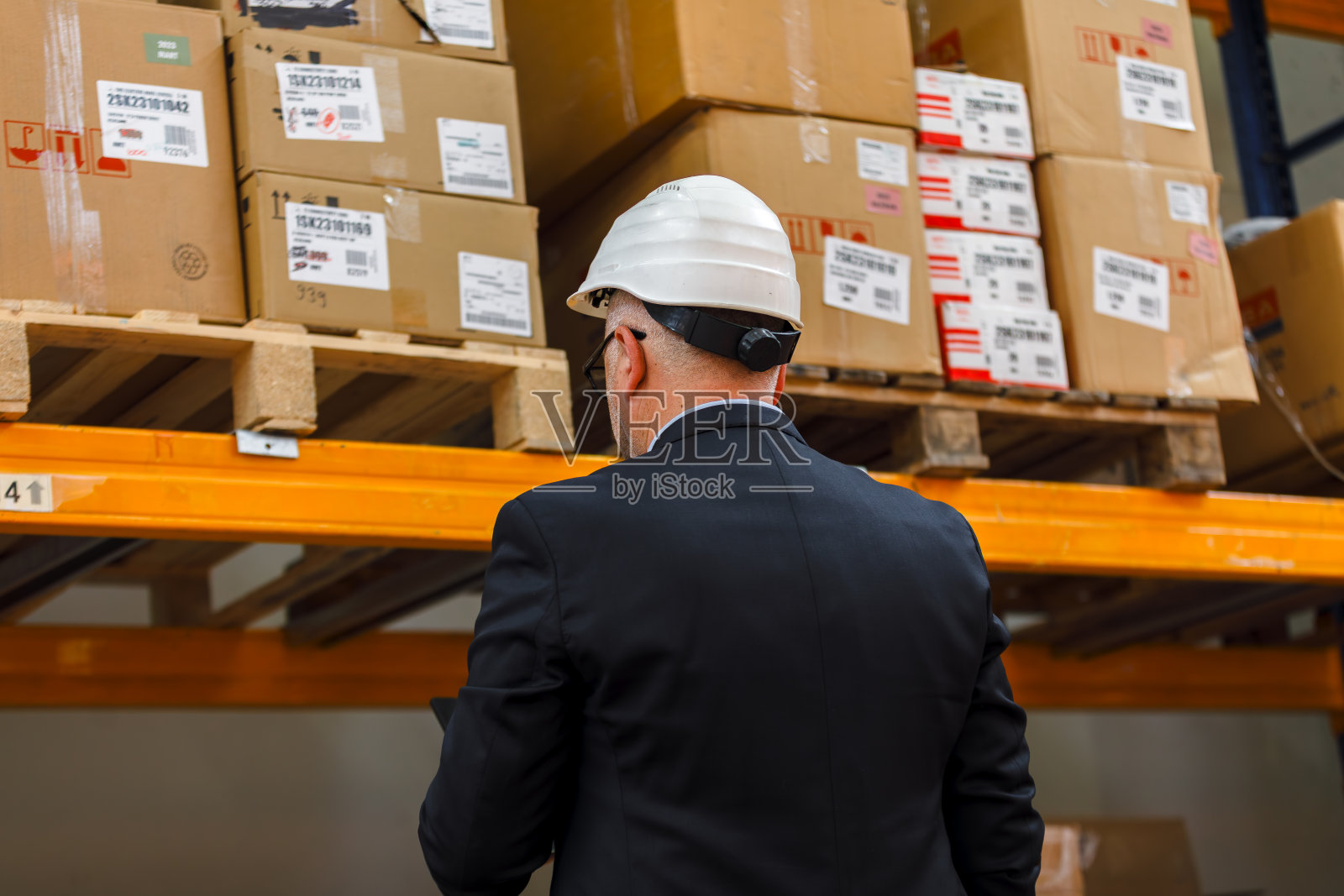 物流仓库中，一位年长的仓库经理在进行库存检查时使用数字平板电脑的背影照片摄影图片