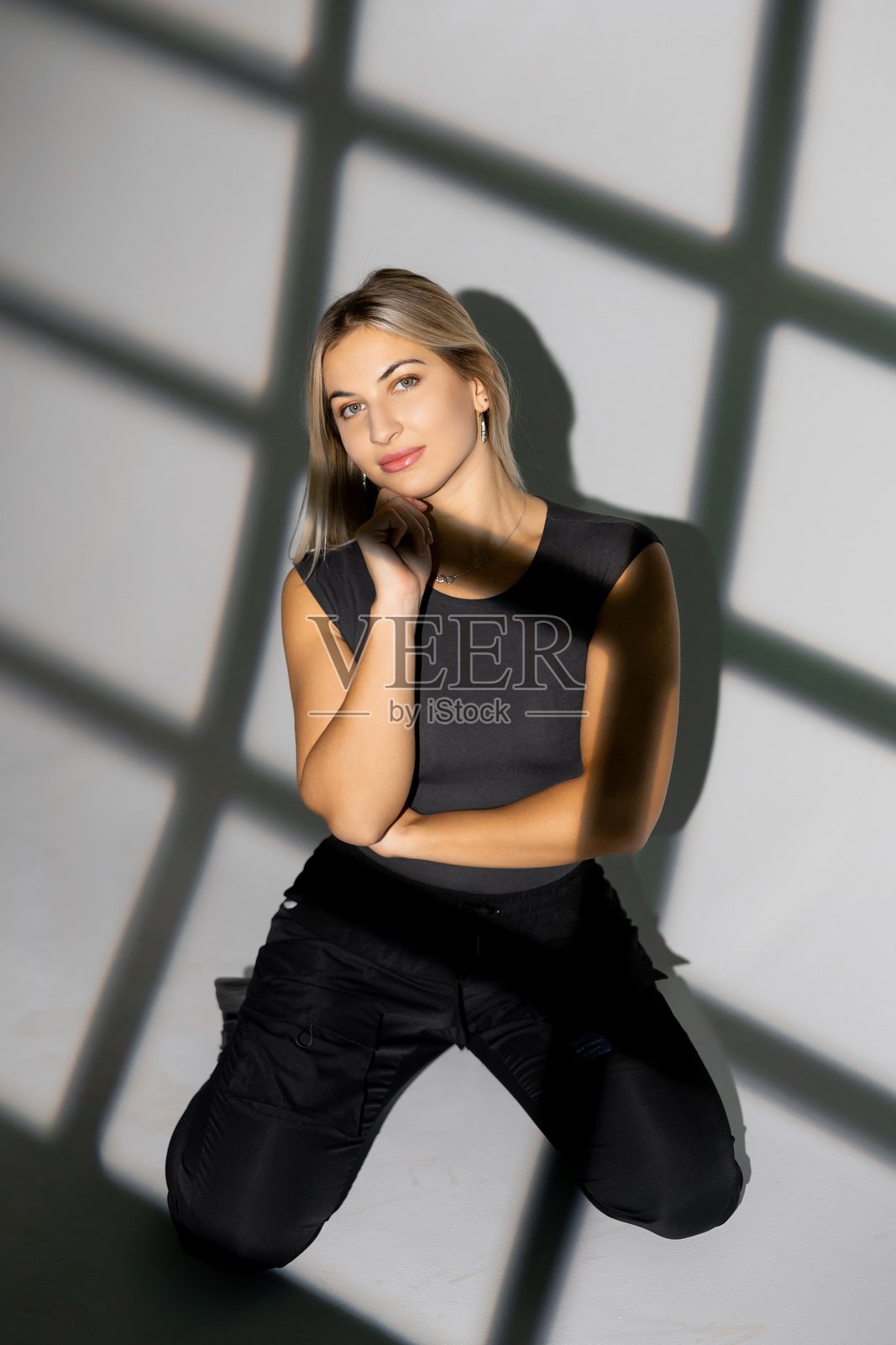 年轻女子跪在地板上摆姿势，窗户的阴影投射在墙上照片摄影图片