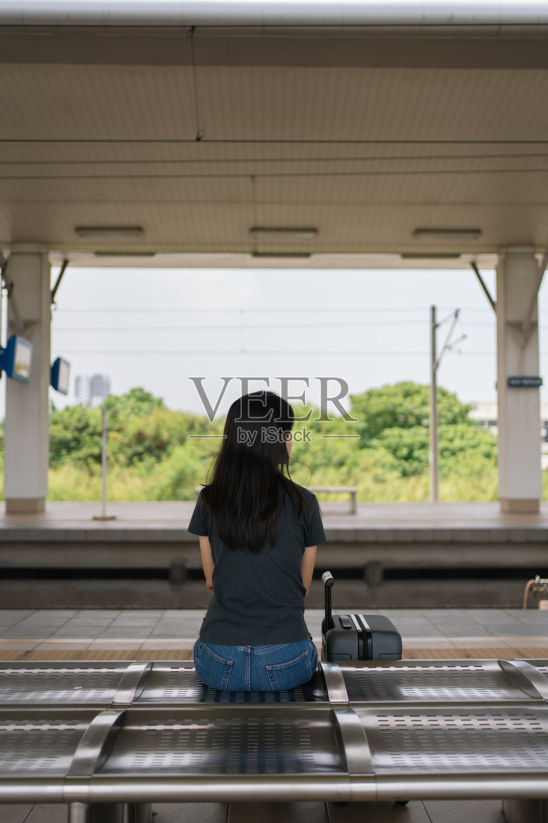 一位女子独自坐在火车站台，面朝轨道，背对着镜头。照片摄影图片