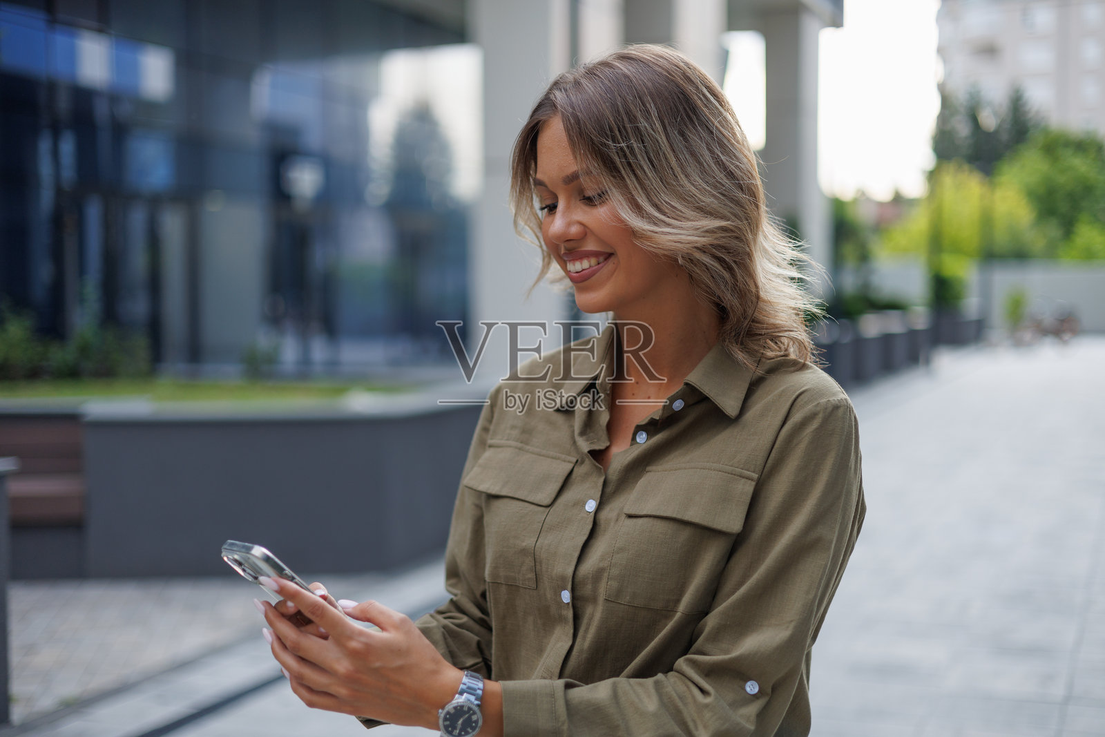 年轻女子在城市户外使用智能手机，面带微笑，可能收到了好消息或正在与人在线交流照片摄影图片