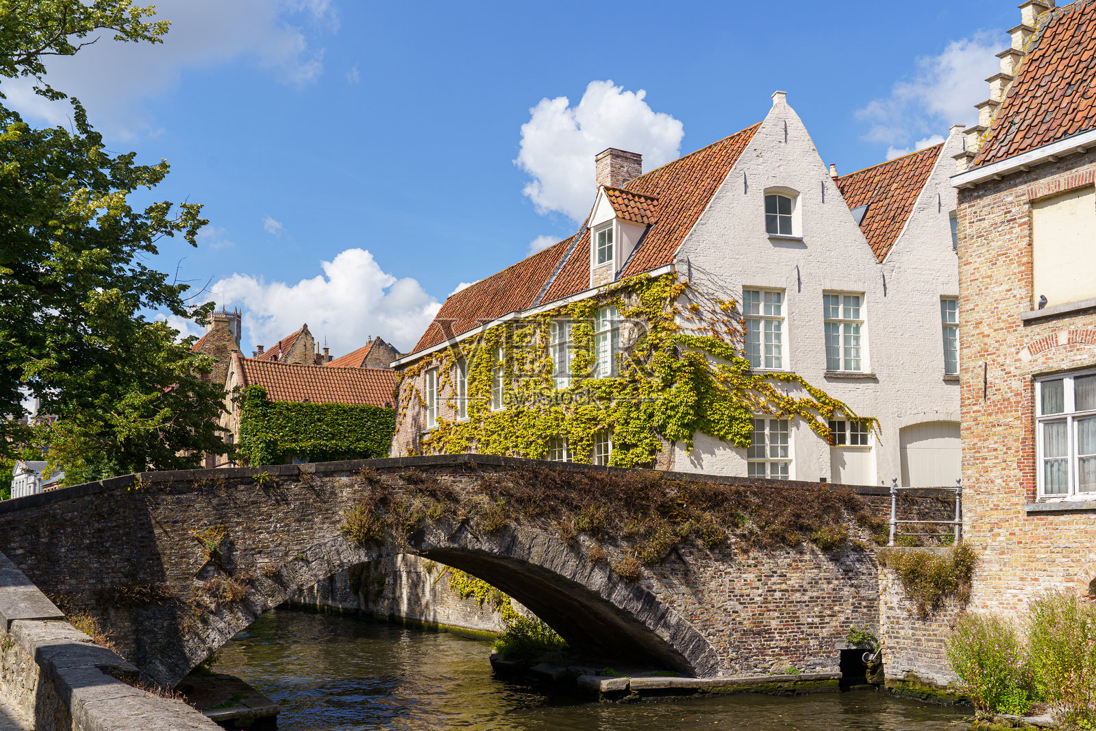 比利时布鲁日，一座桥横跨河流，桥前是排排房屋。这些房屋古老，外观为砖砌。桥梁为石制结构，带有石制栏杆。照片摄影图片