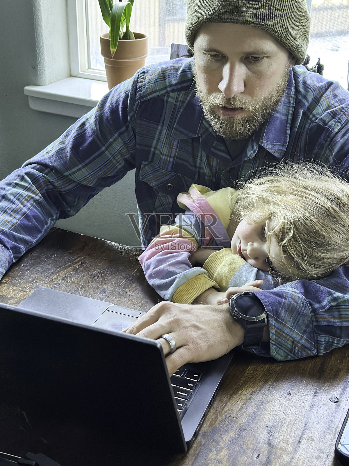 父亲在腿上抱着年幼的女儿，在家远程办公照片摄影图片