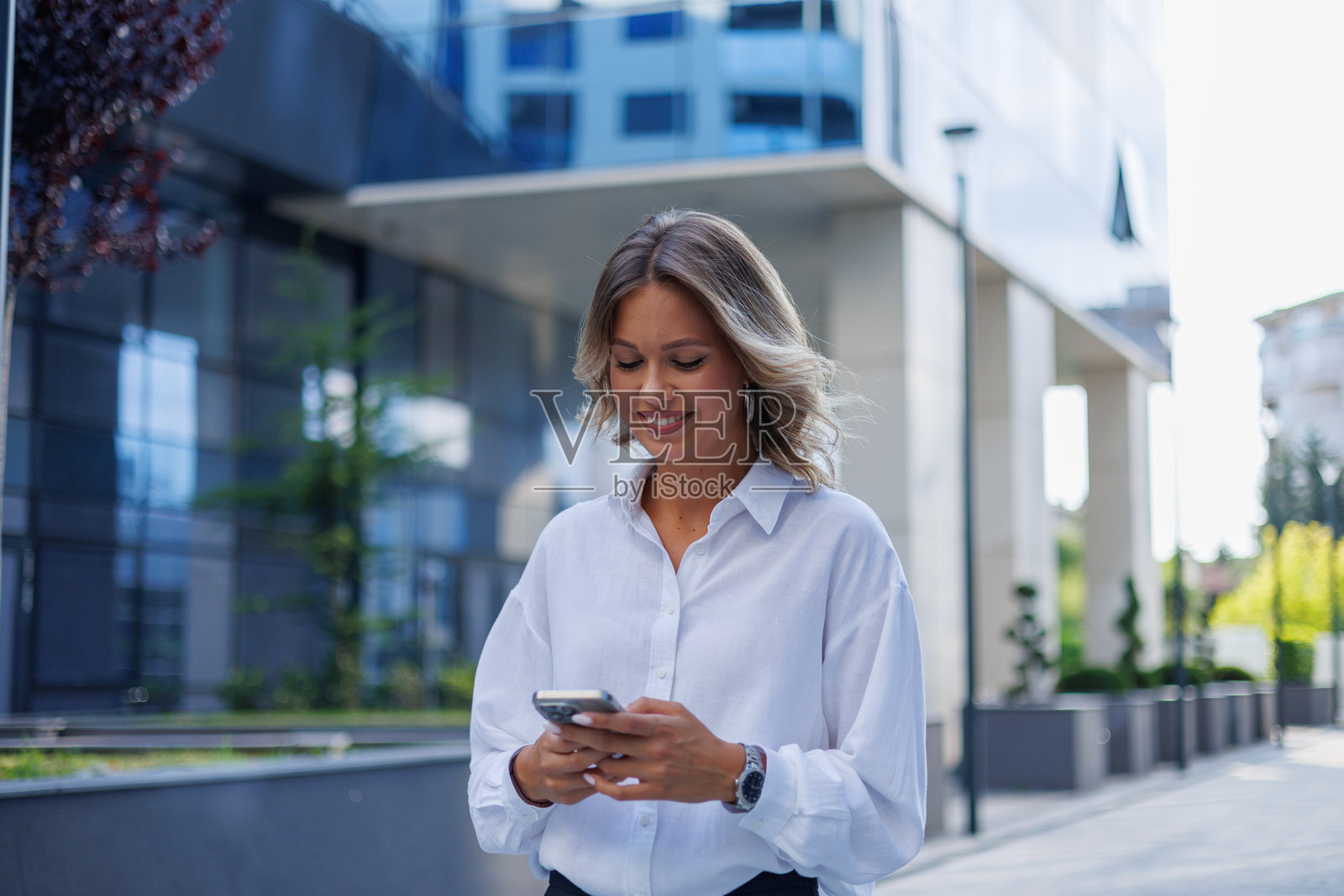 年轻的职业女性在户外使用智能手机进行消息收发、社交媒体互动和商务沟通，背景为城市街景。照片摄影图片