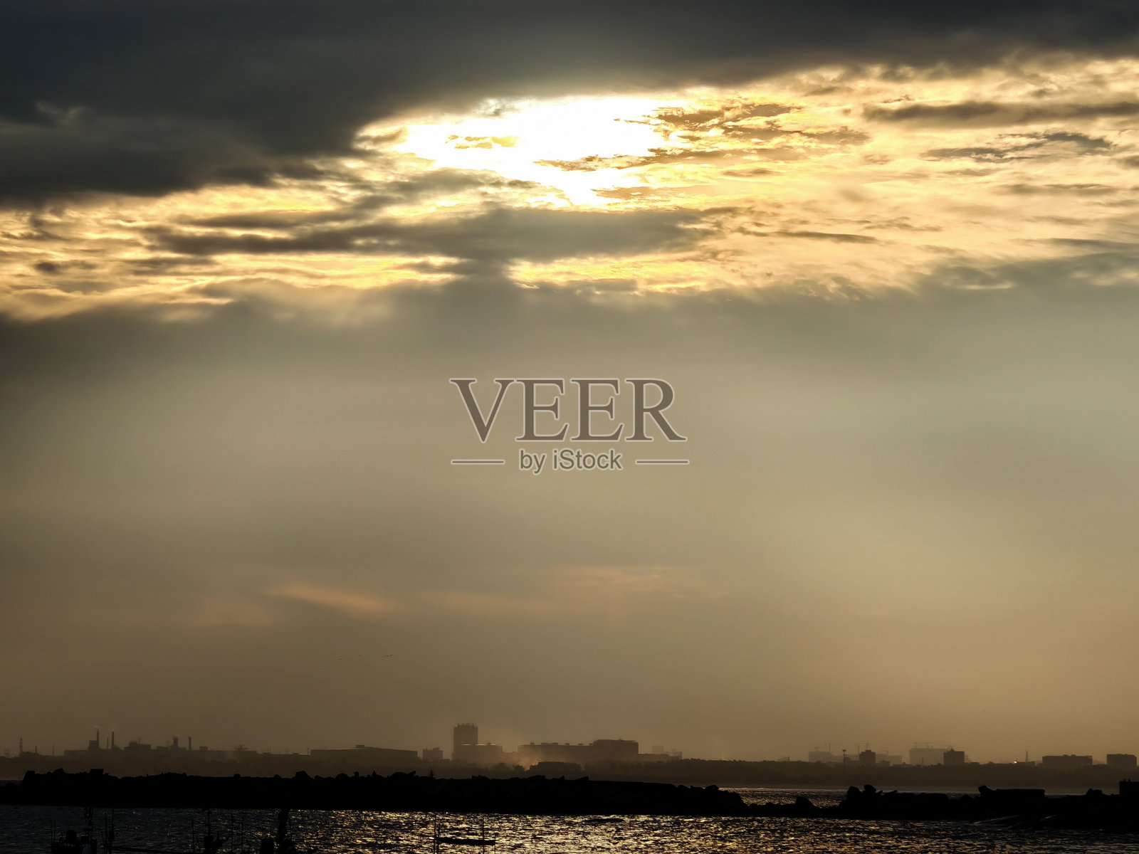 夕阳下的金色光芒穿透云层——水面上的城市剪影照片摄影图片