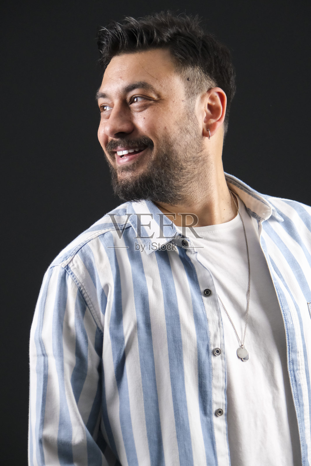 一位富有魅力的中年棕发男子，身着休闲装，在黑暗的黑色影棚背景前摆姿势，灯光戏剧化照片摄影图片