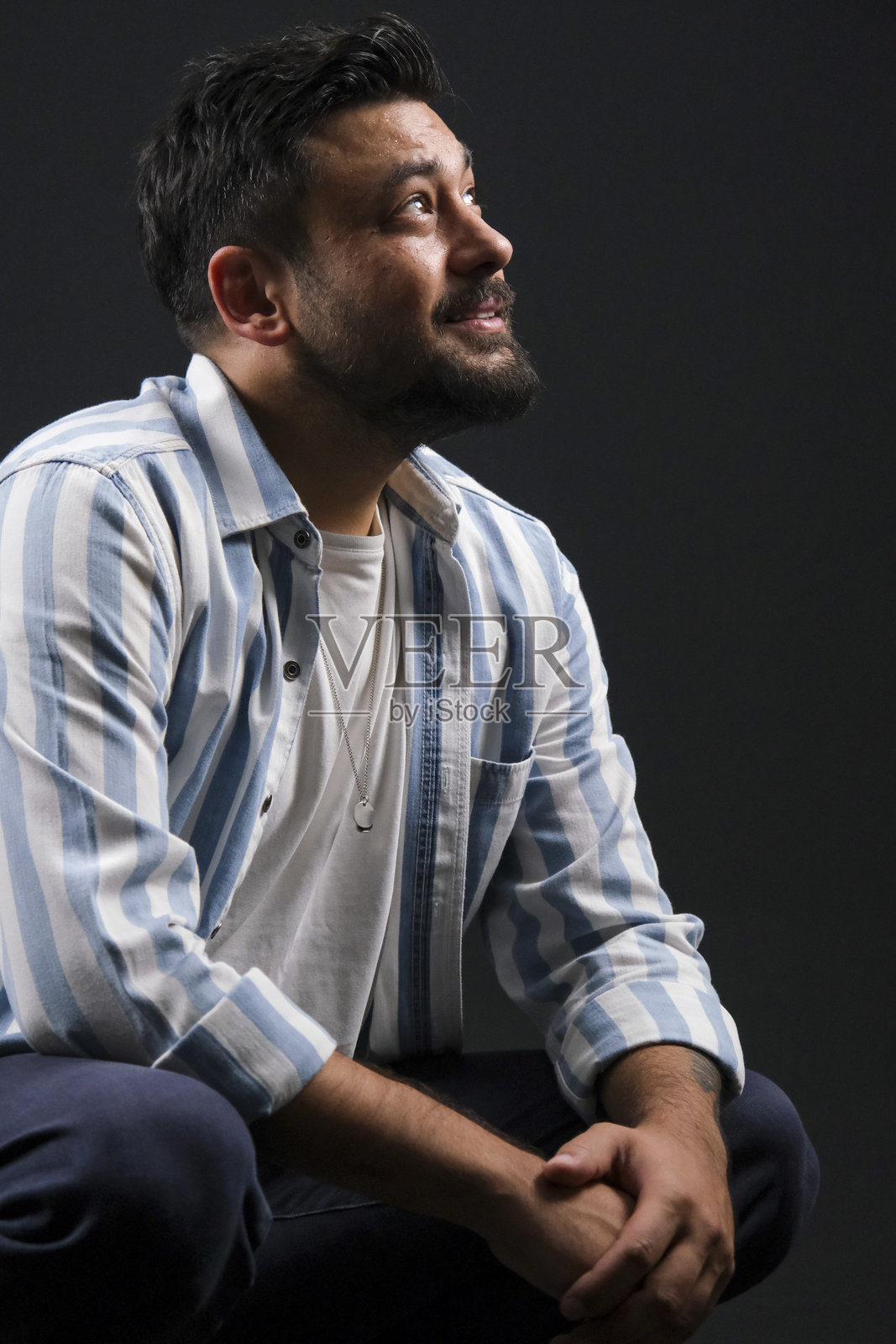 魅力十足的中年深棕色头发男子，身着休闲装，在深黑色影棚背景前摆姿势，灯光富有戏剧性照片摄影图片