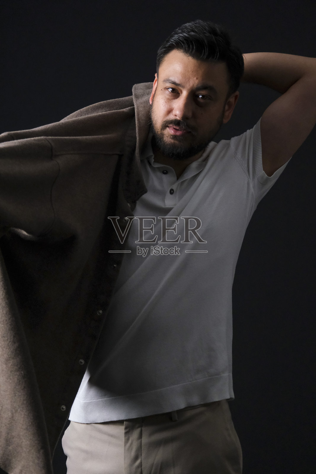 魅力十足的中年棕发男子，身着休闲装，在戏剧性灯光下，于深黑色影棚背景前摆姿势照片摄影图片