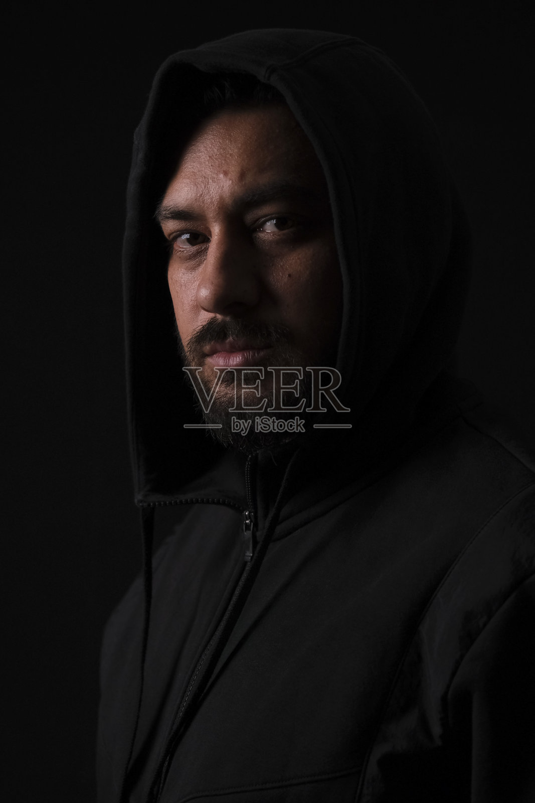 一位迷人的中年棕发男子，身着休闲装，在黑暗的黑色影棚背景前摆姿势，灯光富有戏剧性照片摄影图片