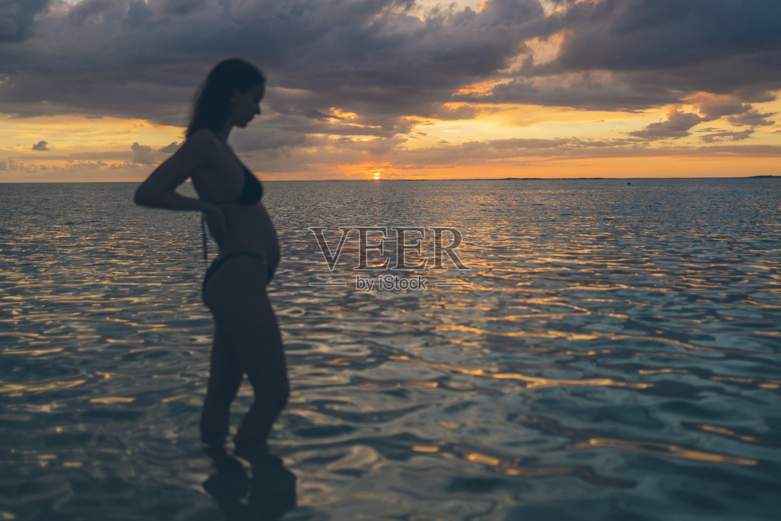 怀孕的女人在日落时分站在浅海中照片摄影图片