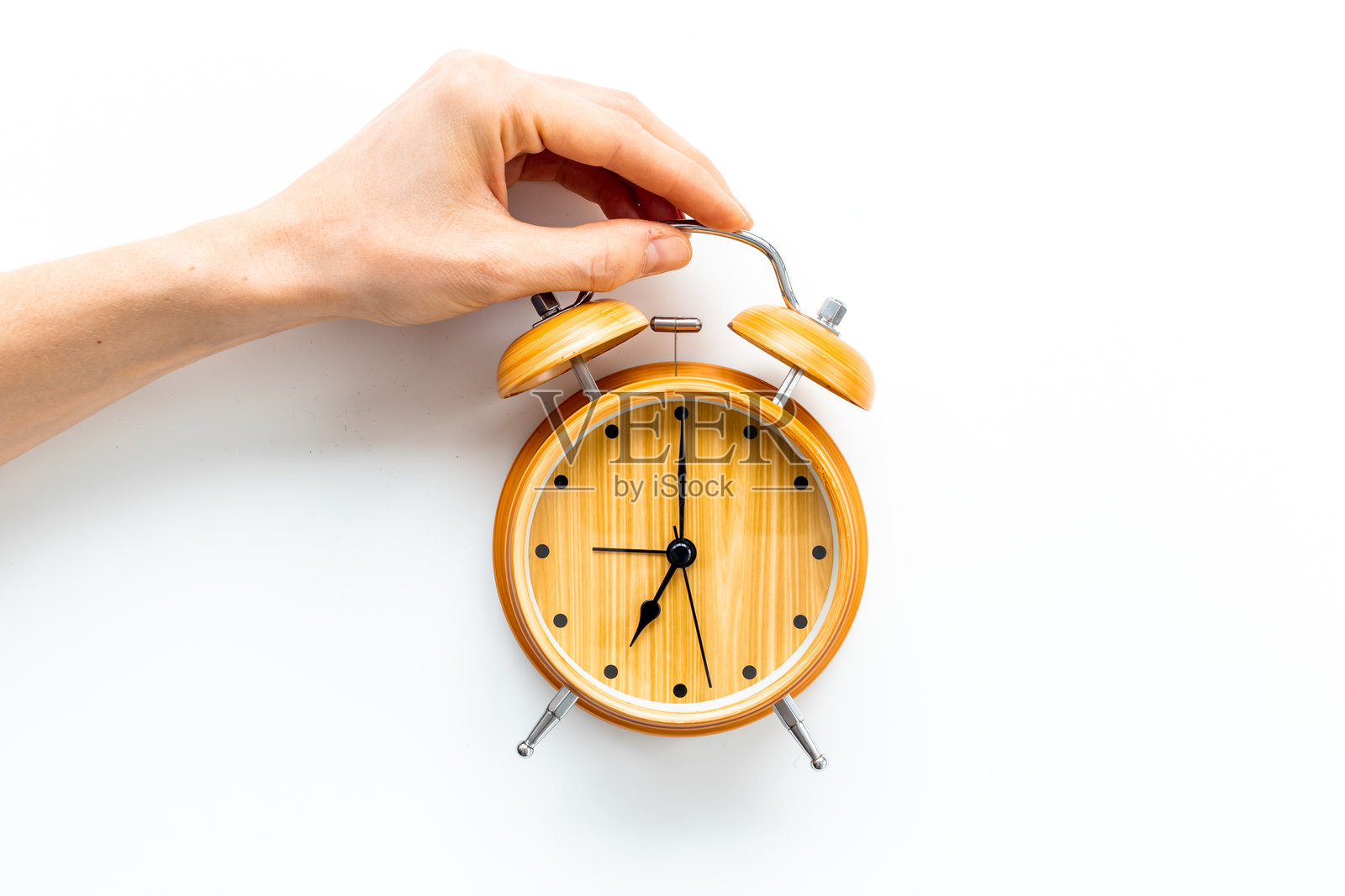 一只手正拿着一个老式木质闹钟，上面有两个铃铛，显示七点。早晨的例行公事。时间概念。照片摄影图片