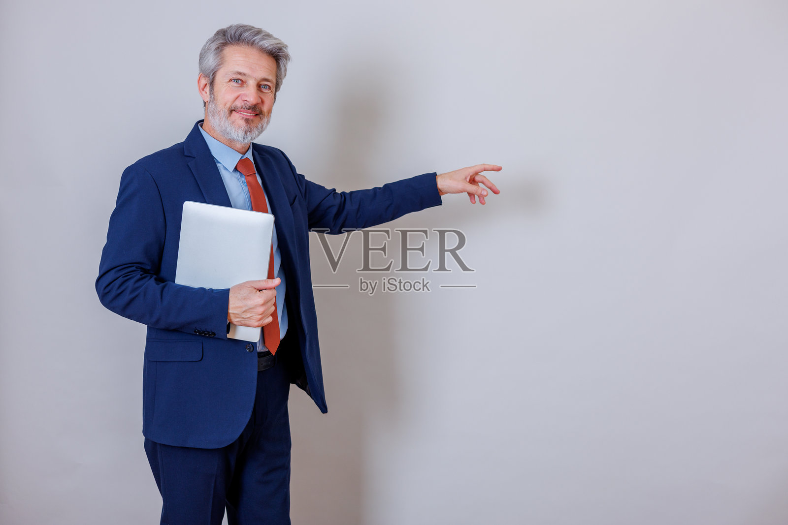 一位面带微笑的成熟商人，手持笔记本电脑，伸出手指指向复印空间，正在展示新想法照片摄影图片