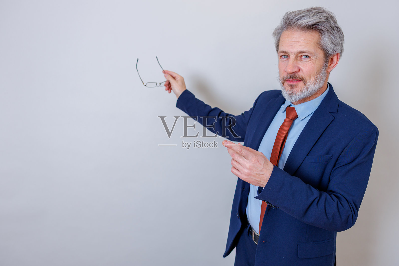 自信成熟的成年商务男士指向复制空间，正在做演示，并拿着眼镜照片摄影图片