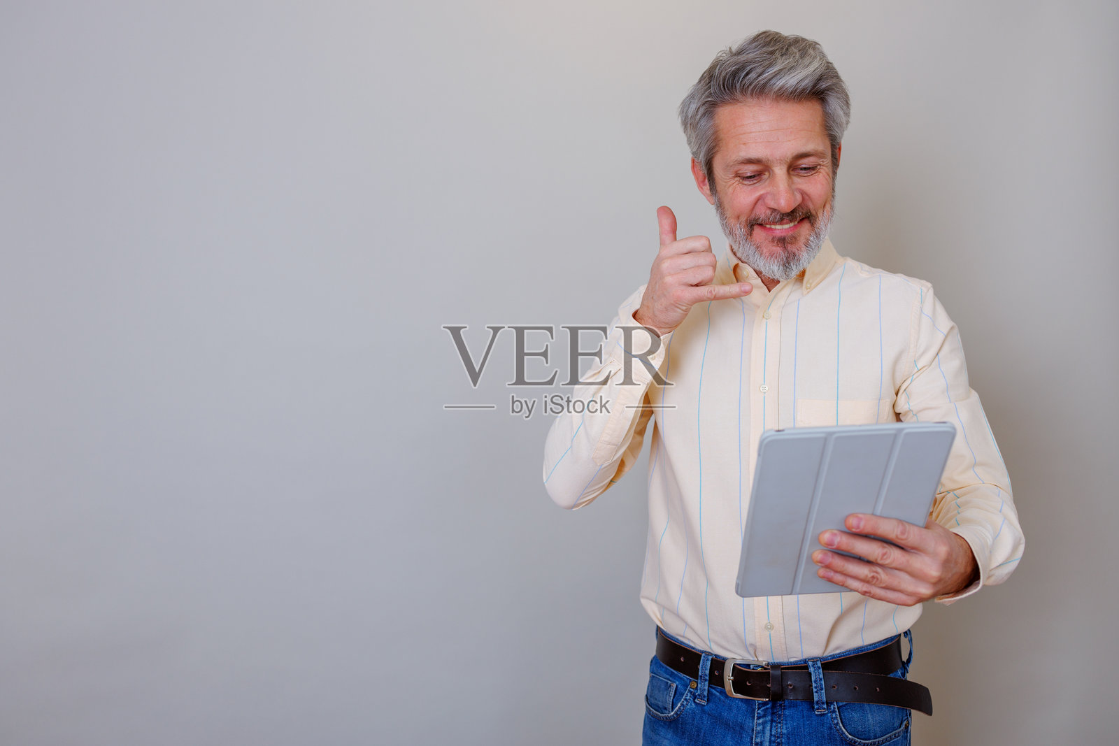 一位中年男子微笑着，手持平板电脑并做出“打电话”手势，正在使用科技进行交流照片摄影图片