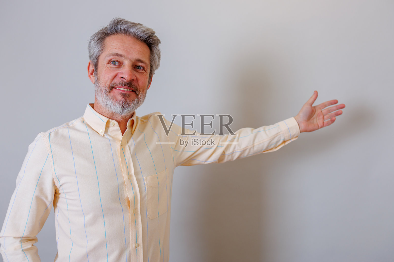 一位头发灰白的中年男子微笑着伸出手，展示新的信息，并留有空白的复制空间照片摄影图片