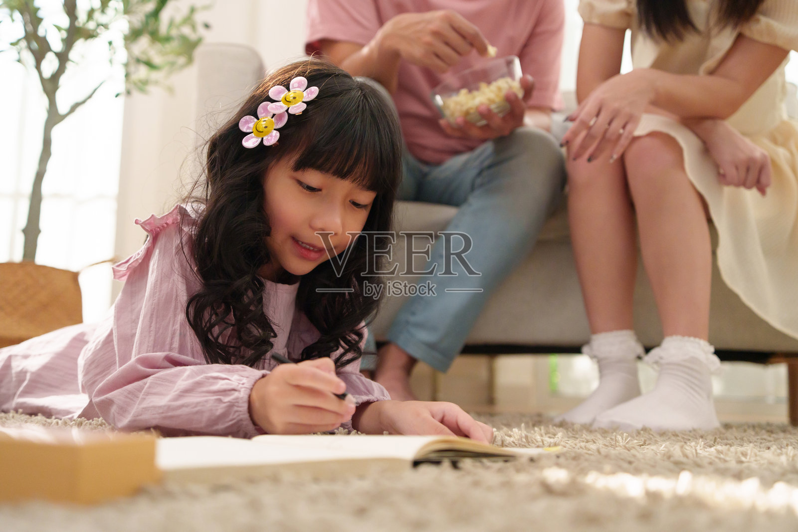 亚洲女孩在地毯上绘画，父母在背景中照片摄影图片