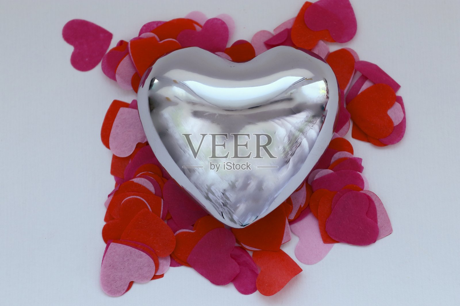 粉色、红色和紫色的纸质心形中，有一个闪亮的金属心形——为情人节打造的浪漫构图。照片摄影图片