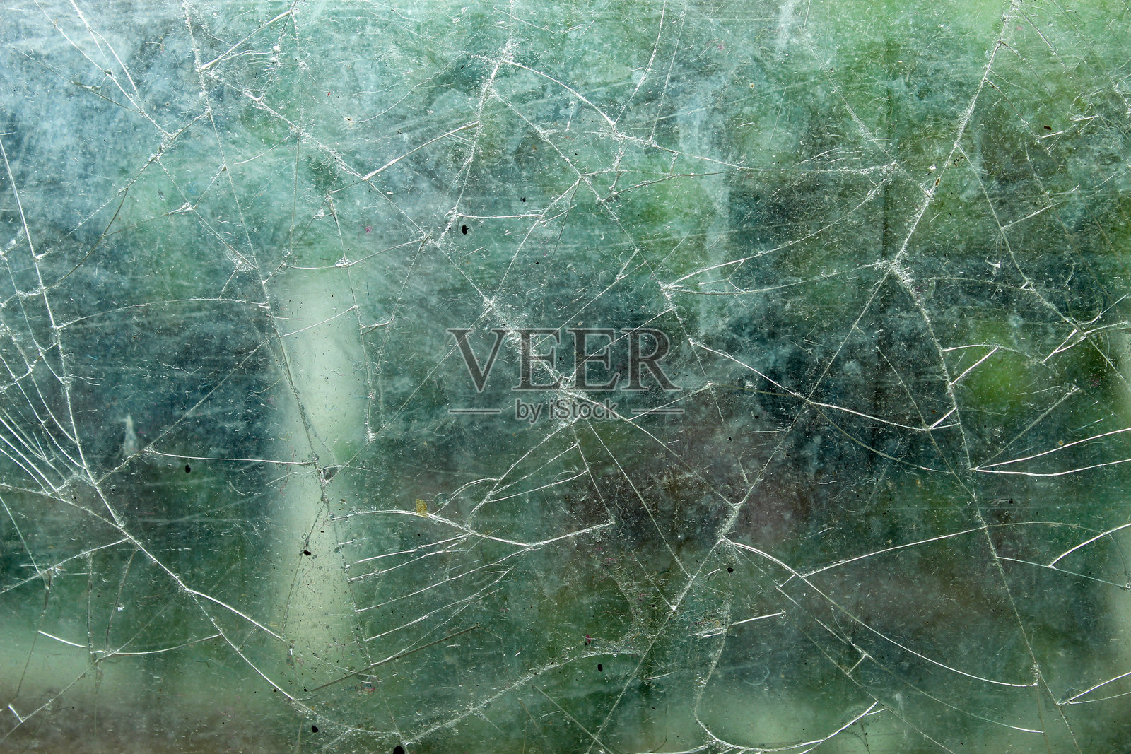 破碎玻璃的纹理。碎玻璃错综复杂的图案在褪色的绿色花园背景下营造出抽象效果。照片摄影图片