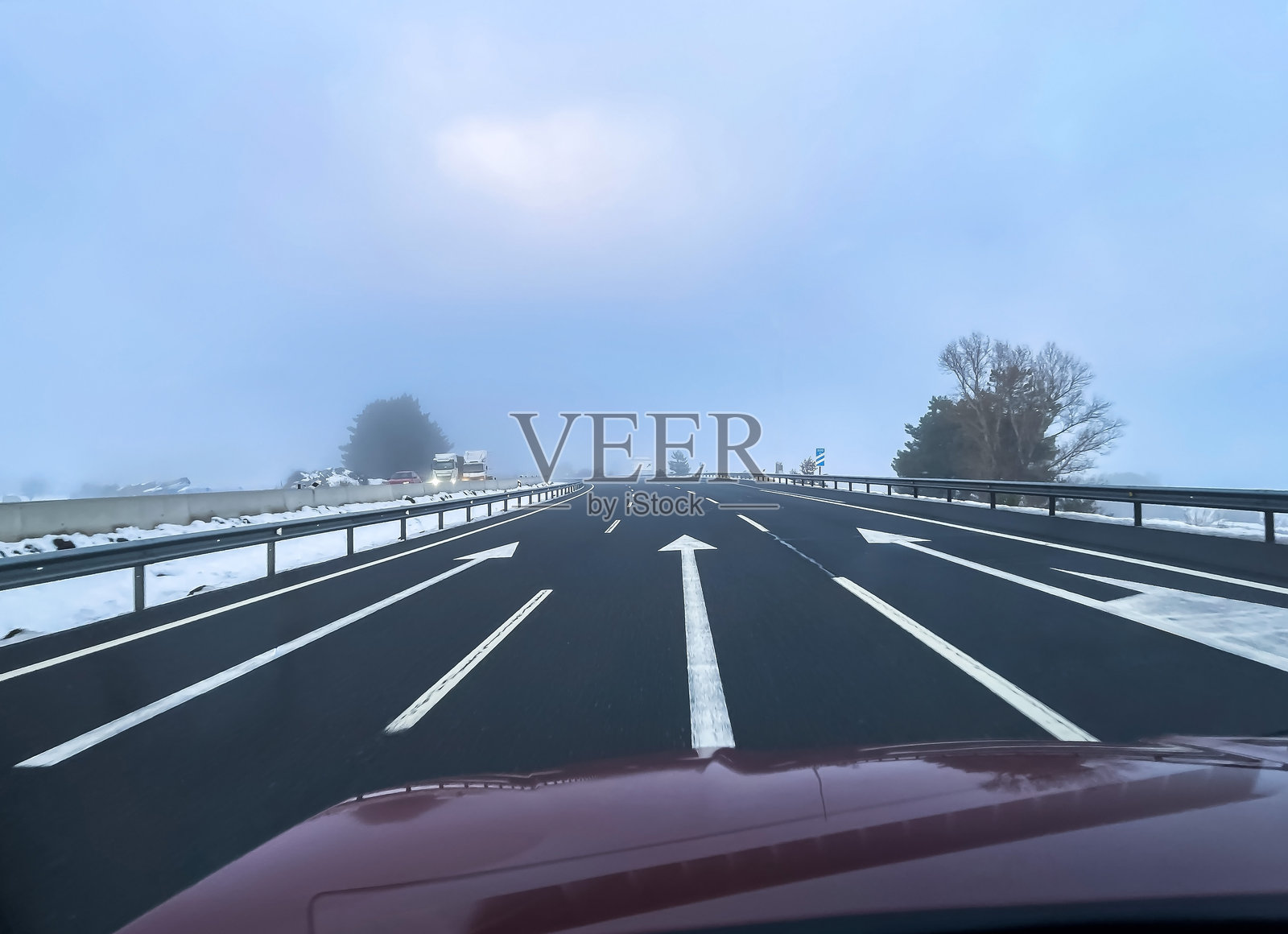 雾气笼罩的高速公路上，车辆行驶中的视角，路肩积雪。深色沥青路面上白色的箭头指向浓雾，下方是寒冷的冬日天空。象征危险驾驶或公路旅行，横向构图照片摄影图片