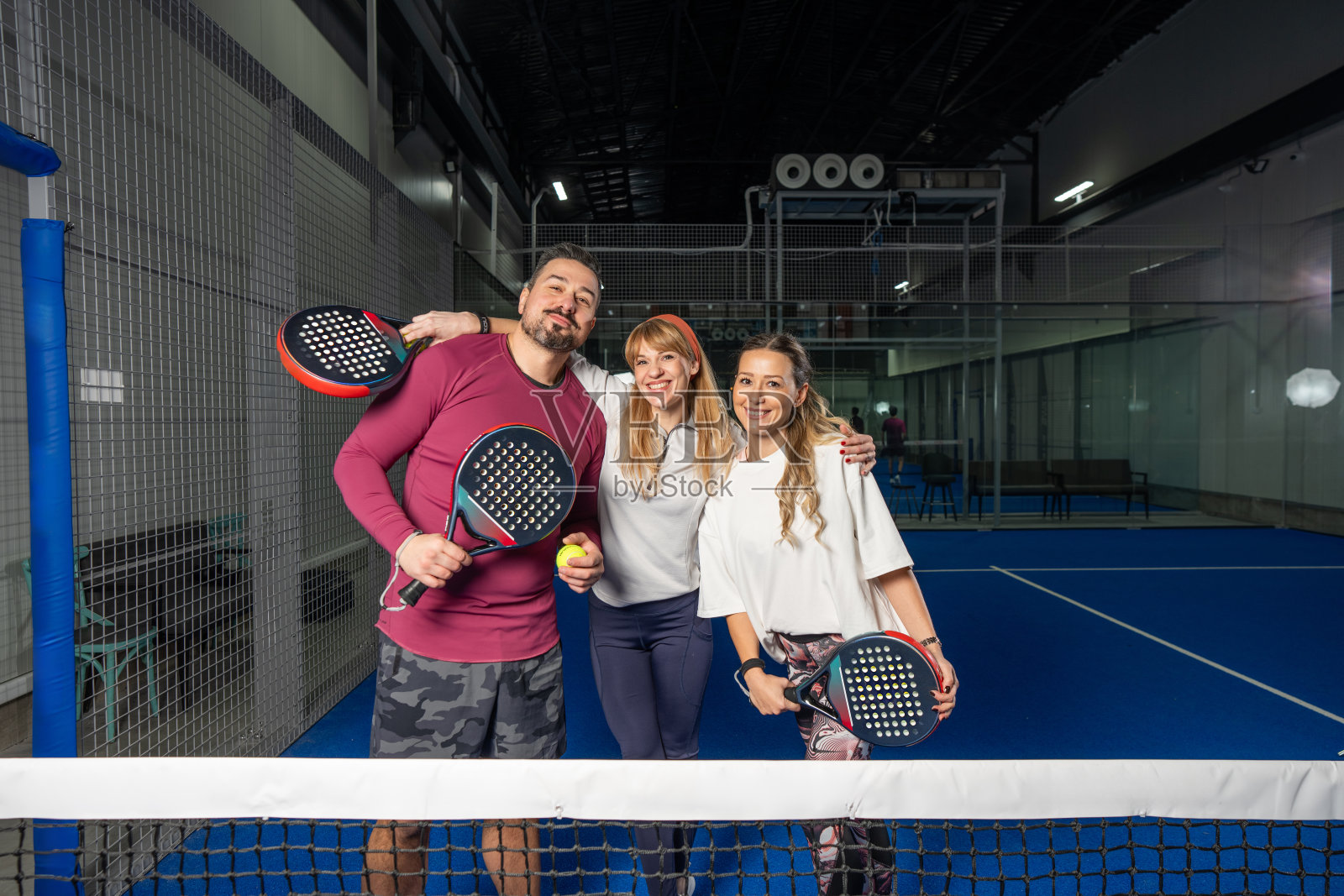 朋友们在室内球场上打板式网球，手持球拍和球，微笑着合影留念照片摄影图片