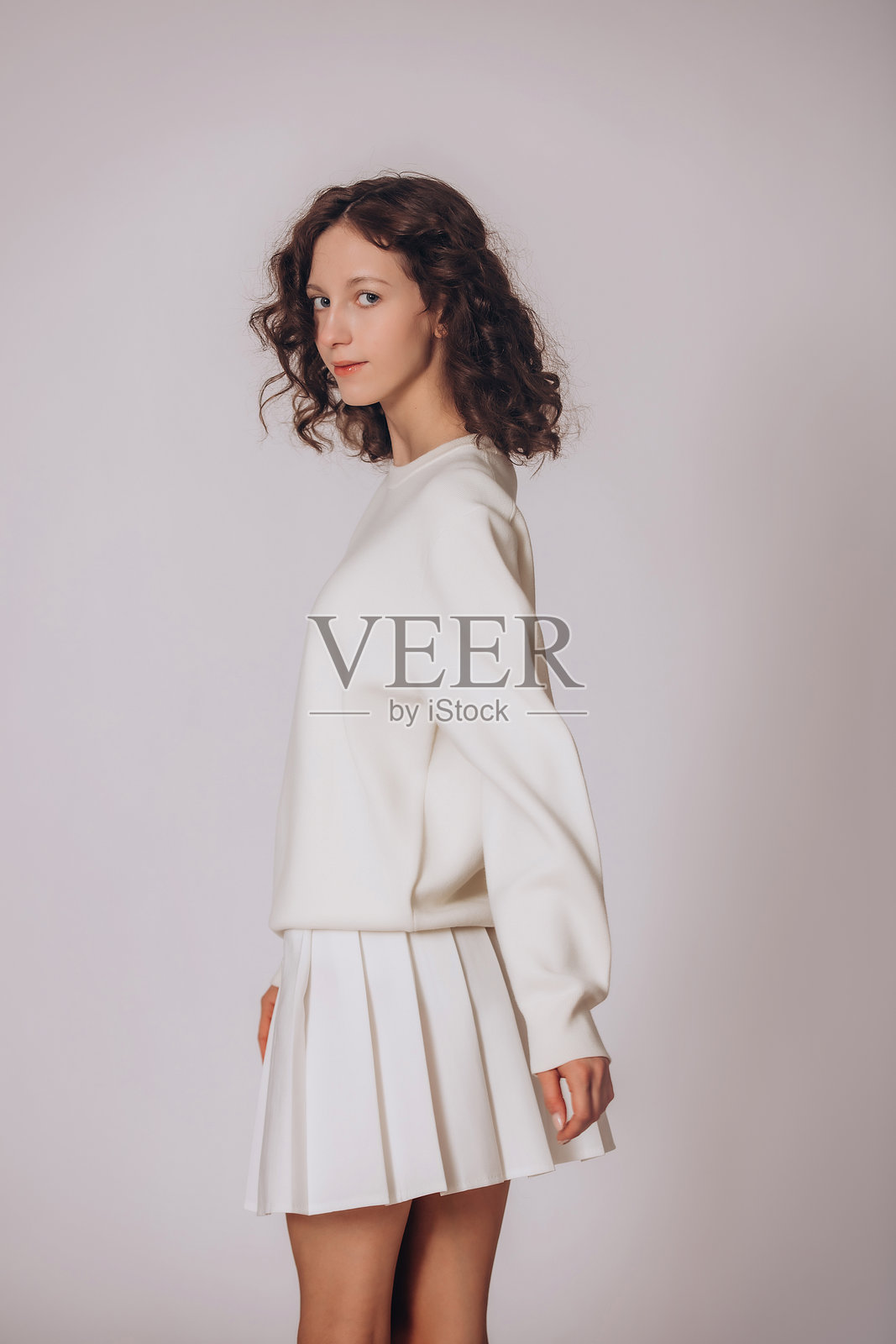 一位年轻美丽的棕发卷发女孩，身穿白色运动衫，背景为白色照片摄影图片