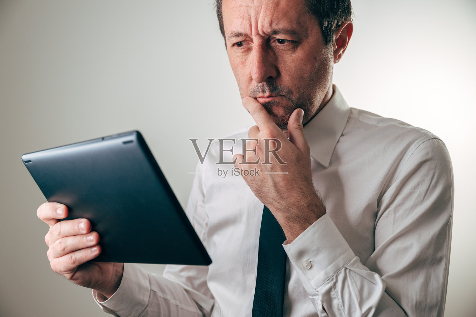身穿白衬衫、系着深色领带的商人，正眉头紧锁地盯着黑色平板电脑上的内容照片摄影图片