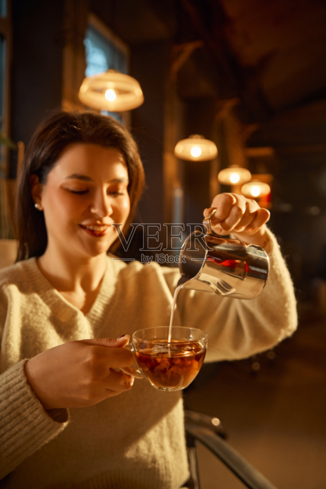 在温馨的咖啡馆内，女子正将牛奶倒入咖啡杯中照片摄影图片