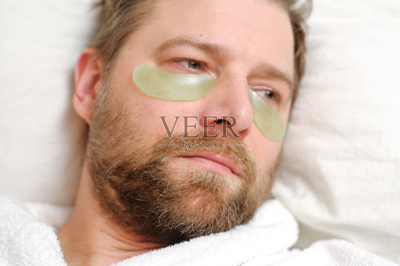 一位英俊的40多岁男子，眼下贴着美容贴片。他早上在护理面部皮肤，正在敷绿色的胶原蛋白贴片。面部护理。美容水疗。眼膜，健康。照片摄影图片