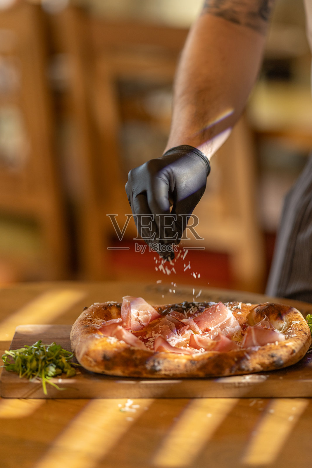 戴着手套的厨师在热披萨上撒上新鲜奶酪，准备上菜照片摄影图片