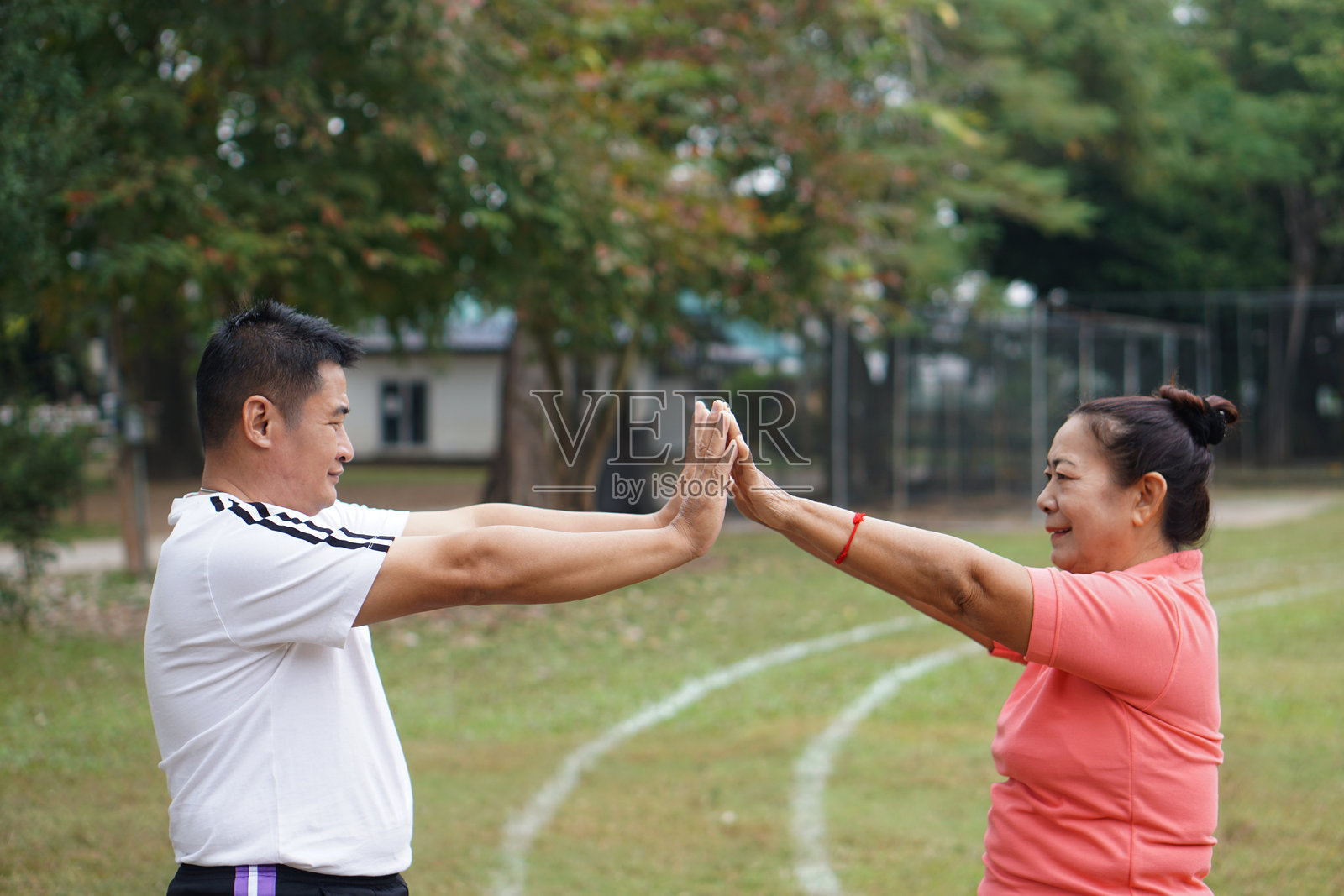 中年亚裔男子与年长亚裔女子在公园一起锻炼，伸展手臂时互相击掌。健康生活方式、家庭活动、健身、养生、幸福、积极老龄化照片摄影图片